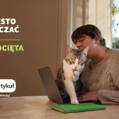 Kobieta z kotem na kolanach przed laptopem, kot liże łapkę.