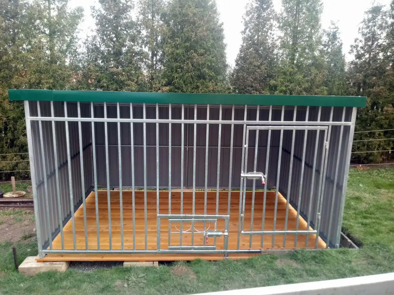 Gotowy kojec dla psa z paneli ogrodzeniowych, z drewnianą podłogą i zielonym dachem. Idealny, gdy zastanawiasz się, jak zrobić kojec dla psa z paneli ogrodzeniowych.