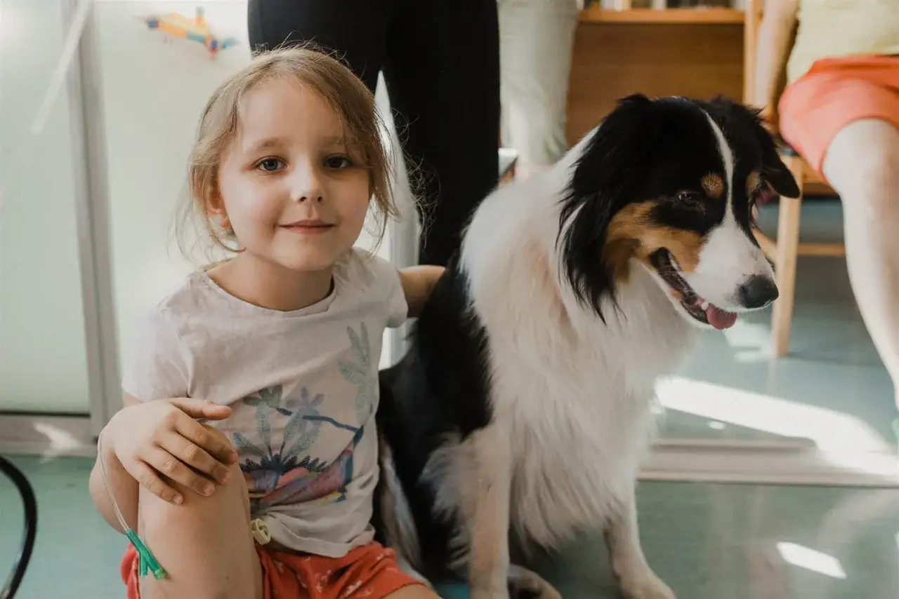 Uśmiechnięta dziewczynka z pieskiem, który jest jej towarzyszem w dogoterapii.